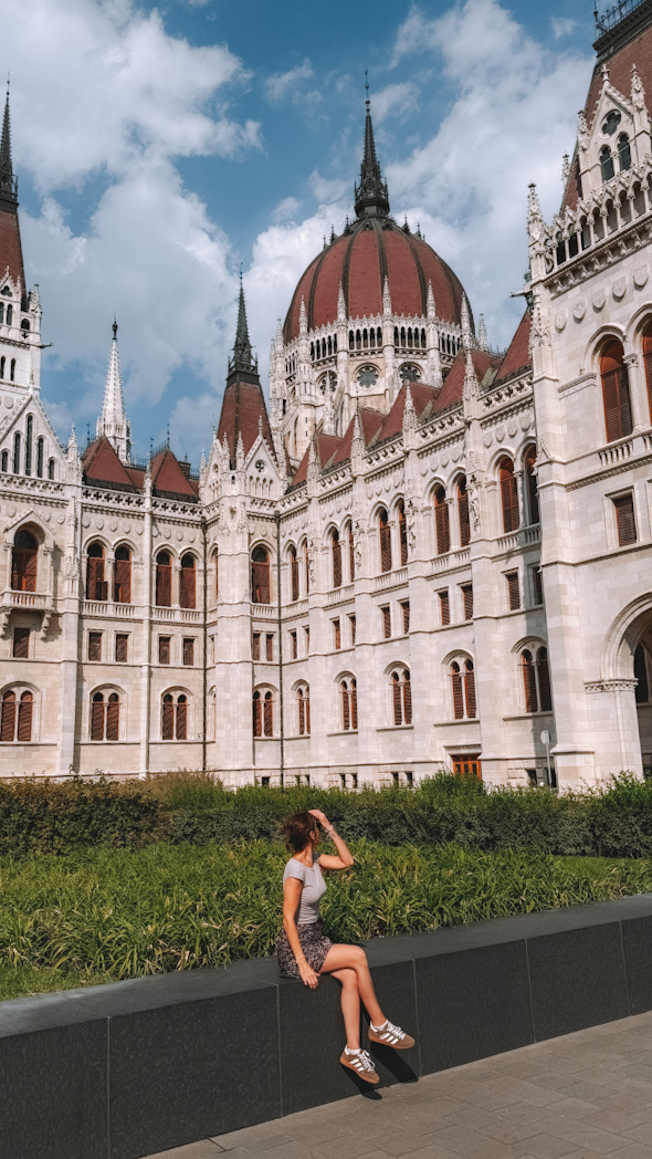 Femme posant devant la façade imposante du Parlement hongrois à Budapest